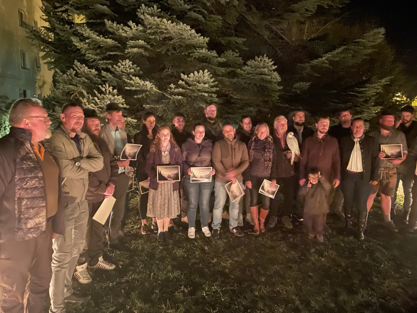 Jagdschule Hunters World: Absolventengruppe mit Greifvogel und Urkunden bei der Abschlussfeier am Abend