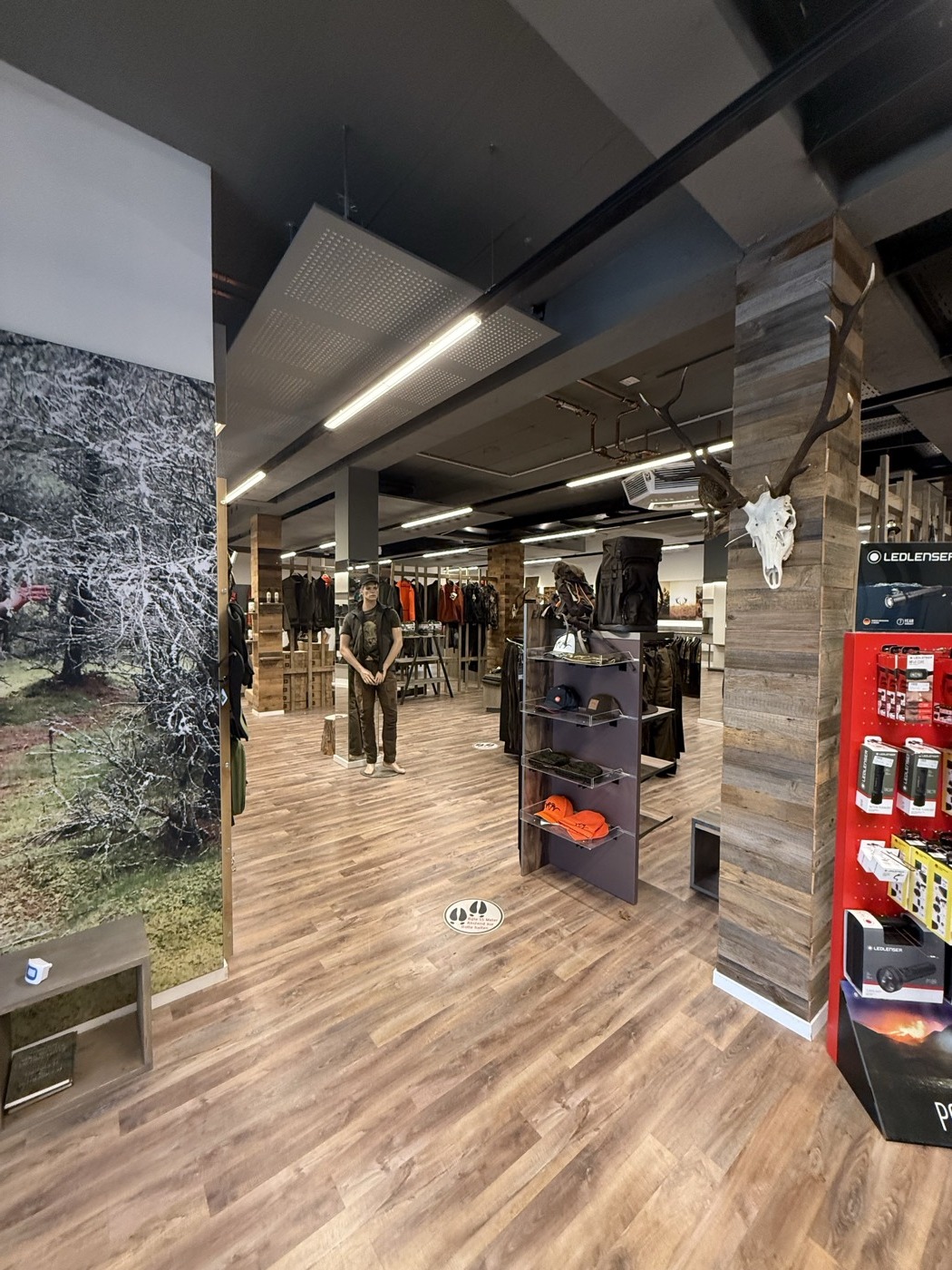Jagdshop-Verkaufsraum mit Jagdbekleidung, Naturfoto und Geweih an der Wand